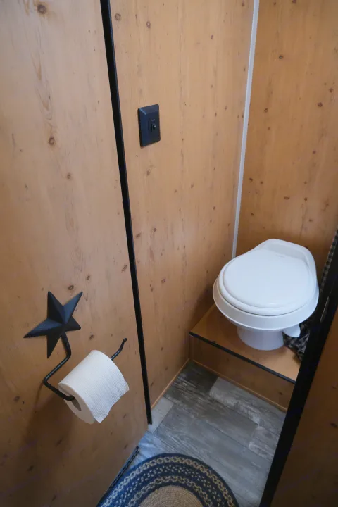 Compact RV rental bathroom: light wood walls, white toilet, dark flooring, and a star-themed toilet paper holder.. Sunray Sunlite 16BH 2023