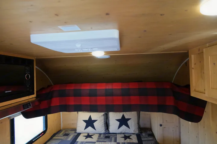 Cozy RV rental interior: bed with plaid blanket, microwave & wood accents.. Sunray Sunlite 16BH 2023