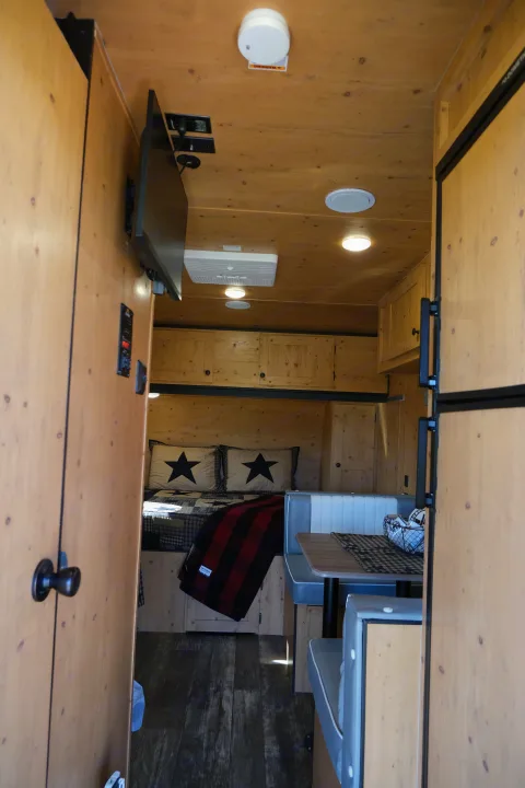 Cozy RV rental interior: wood-paneled walls, bed with star pillows, dinette, TV, and fridge.. Sunray Sunlite 16BH 2023