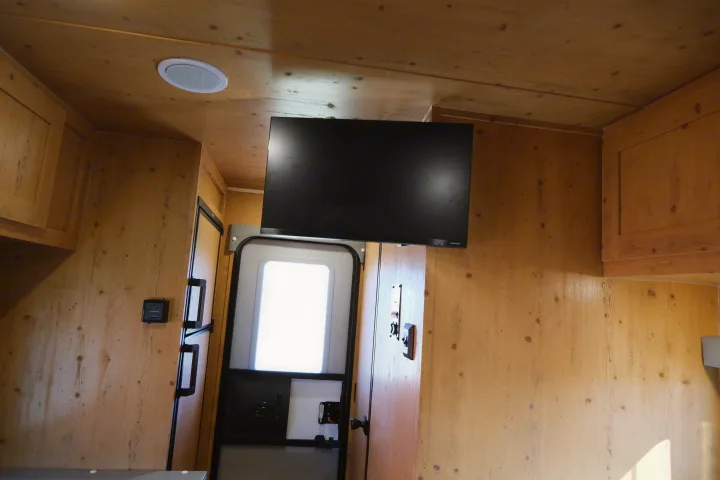 Inside an RV rental, featuring warm wood paneling, a ceiling speaker, mounted TV, and a bright exit door.. Sunray Sunlite 16BH 2023