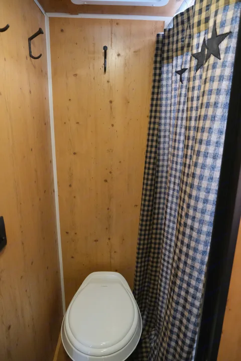 RV rental bathroom features light wood walls, a Dometic toilet, and a blue and white checkered shower curtain with star accents.. Sunray Sunlite 16BH 2023