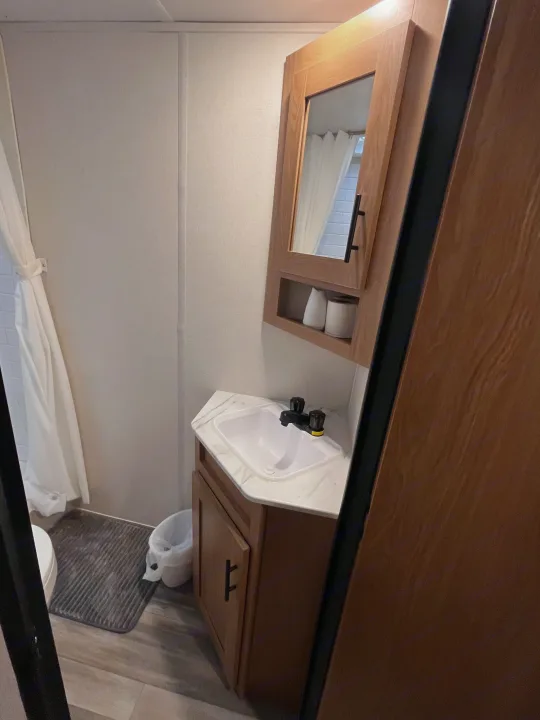 Compact RV rental bathroom featuring a vanity with sink, mirrored cabinet, and a white shower curtain next to the toilet.. Forest River Prime Time Avenger 27 DBS 2023