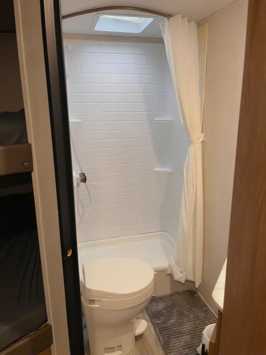 Experience the compact, functional bathroom and shower setup inside this RV rental, featuring a toilet and adjacent bunk beds.. Forest River Prime Time Avenger 27 DBS 2023
