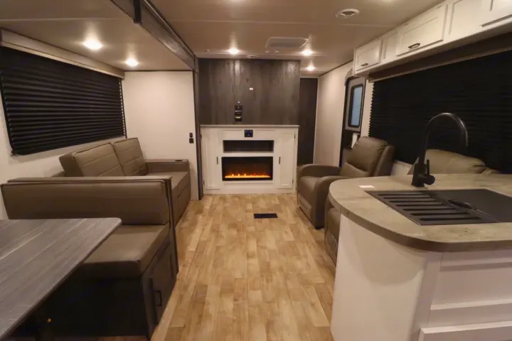 Modern RV rental interior showcasing a cozy living area with recliners, sofa, dining nook, kitchen with sink, and electric fireplace.. Keystone RV Hideout 2023