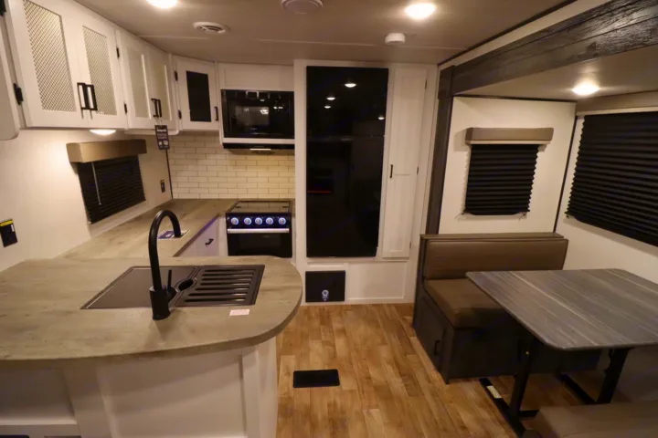 Modern RV rental kitchen with compact dining area. Features include stove, fridge, and stylish finishes, ideal for travel.. Keystone RV Hideout 2023