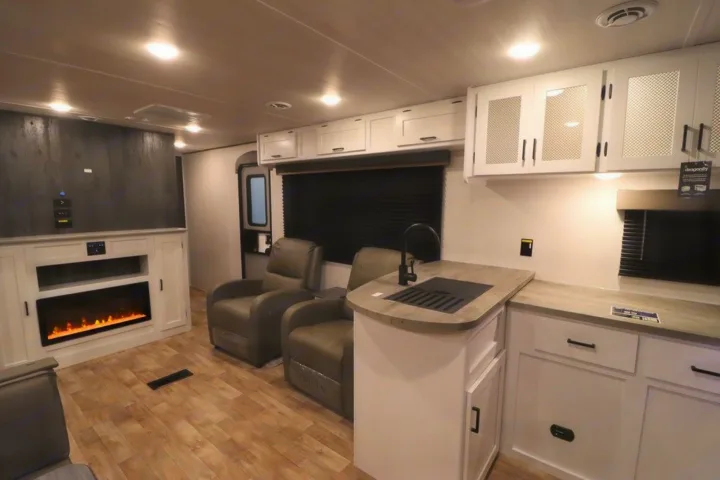 This modern RV rental interior offers a comfortable living space with an electric fireplace, recliner chairs, and a well-equipped kitchenette.. Keystone RV Hideout 2023
