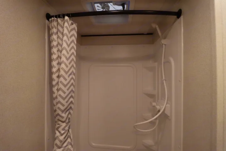 Compact RV rental shower: chevron curtain, handheld showerhead, built-in shelves, and ceiling fan for travel comfort.. Keystone RV Hideout 2023