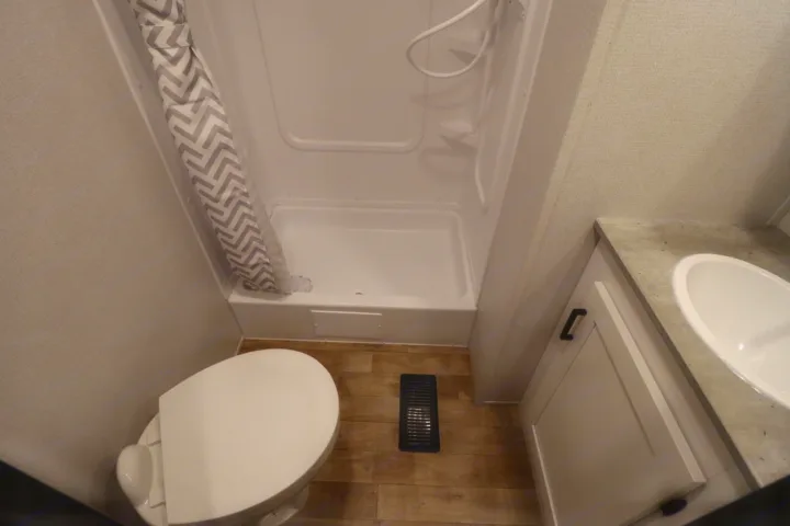 Inside an RV rental: a compact bathroom with white toilet, zigzag shower curtain, and sink vanity.. Keystone RV Hideout 2023