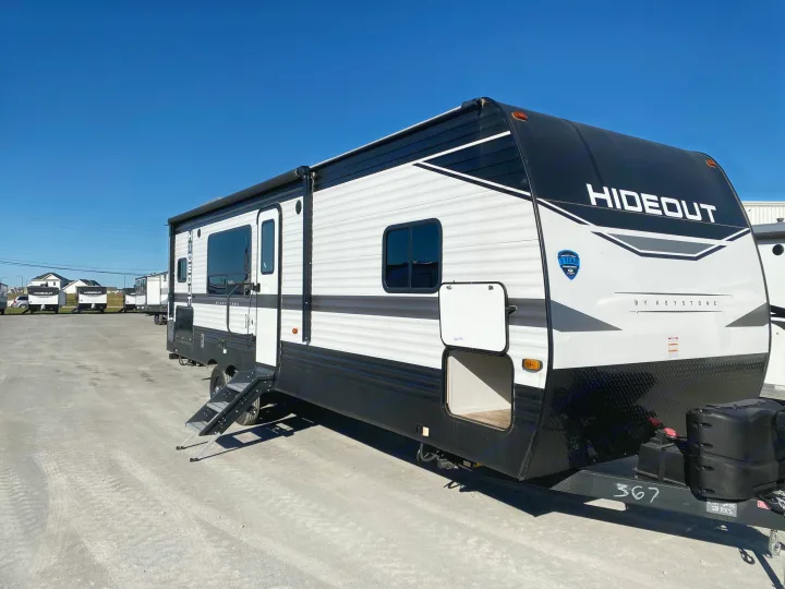 A white and black Hideout travel trailer, perfect for an RV rental, sits on an outdoor lot under a clear blue sky. Ready for adventure.. Keystone RV Hideout 2023