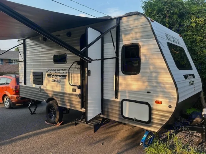 Light-colored Sportsmen Classic travel trailer shown with awning extended and steps down, available for RV rental.. KZ Classic 2022
