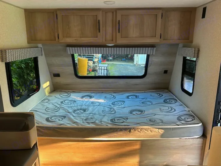 RV rental bedroom interior featuring a comfortable mattress, overhead cabinets, and bright windows.. KZ Classic 2022
