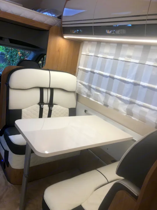 Inside a bright **rv rental**: dining table, cozy black/white seating, overhead bed, and ample storage. Perfect for travel.. Roller Team Auto Roller 746 2023
