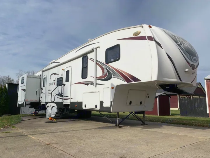 White Sabre fifth-wheel RV parked on a driveway with slide-outs extended, ideal for an RV rental getaway.. Forest River Palomino Sabre 2015