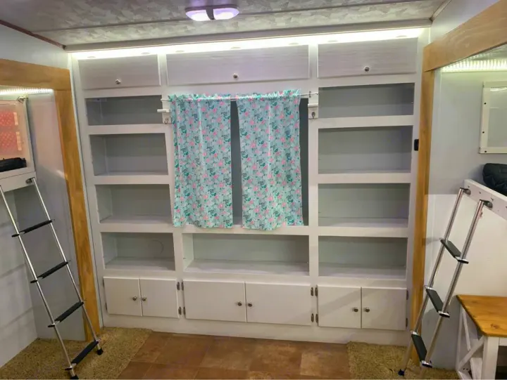 RV rental interior: White built-in storage with open shelves, cabinets, and a floral curtain. Bunk bed ladders flank. Compact, functional.. Forest River Palomino Sabre 2015