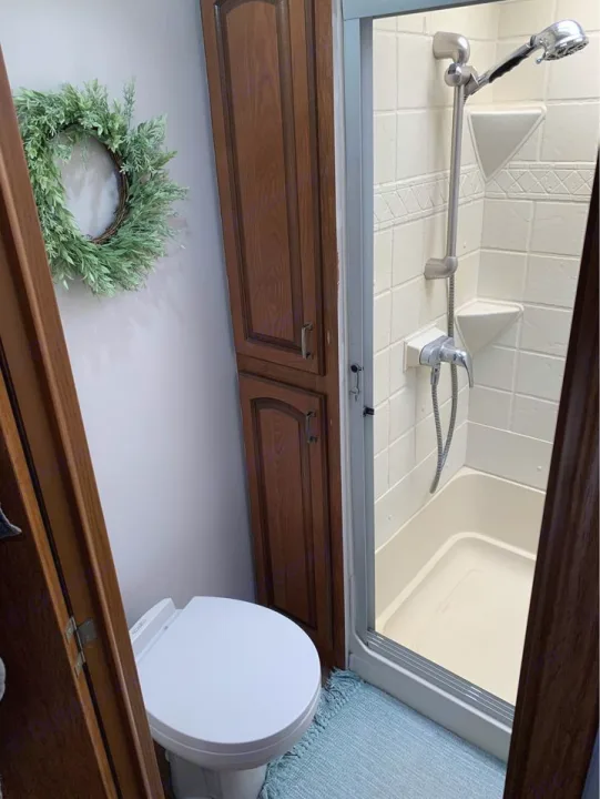 Inside an RV rental bathroom: compact toilet, shower stall, and storage cabinet. A green wreath and blue rug add charm.. Forest River Palomino Sabre 2015