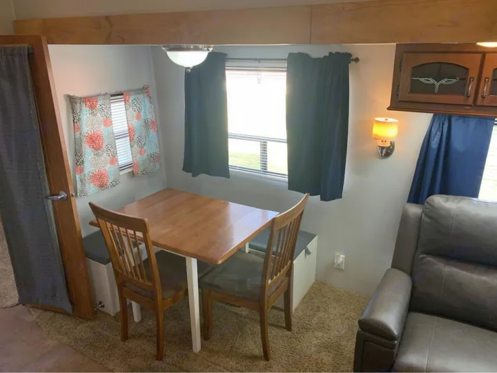 An inviting RV rental interior featuring a dining booth with table, chairs, windows, and a comfortable sofa.. Forest River Palomino Sabre 2015