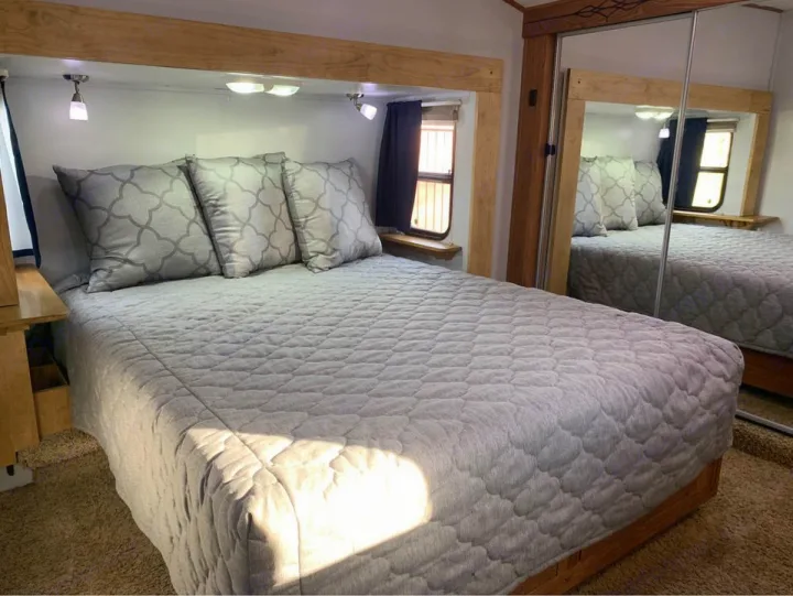 Comfortable RV rental bedroom featuring a queen bed with soft grey quilted bedding and a mirrored closet.. Forest River Palomino Sabre 2015