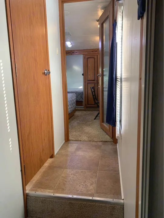 A narrow hallway with tile flooring leads to a cozy carpeted bedroom area in an RV rental, showing interior features.. Forest River Palomino Sabre 2015