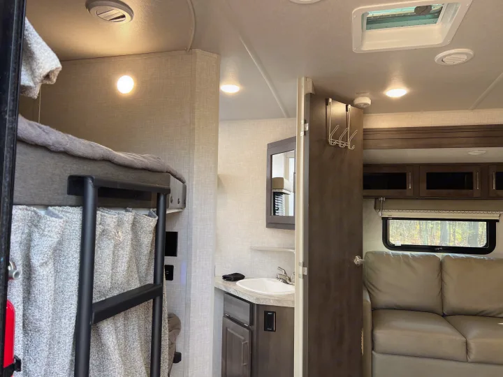 This RV rental interior features bunk beds, a compact bathroom with a sink, and a comfortable living area with a sofa.. Forest River Flagstaff Super Lite 2021