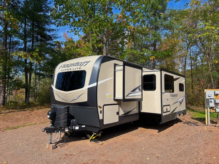 Beige Flagstaff RV rental travel trailer set up on a gravel campsite amidst fall foliage.. Forest River Flagstaff Super Lite 2021