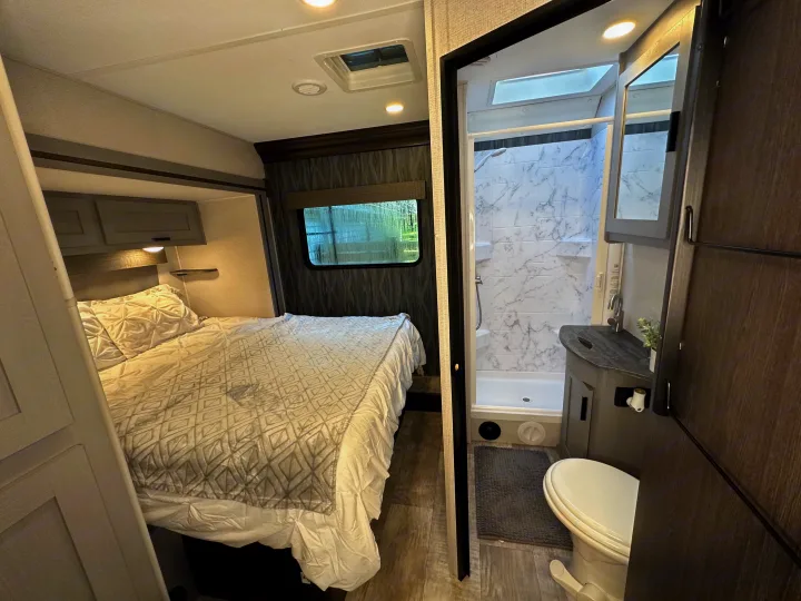 RV rental interior: cozy bedroom with bed & window, beside a full bathroom with shower, sink & toilet. Perfect for travel.. Forest River Solera 2021