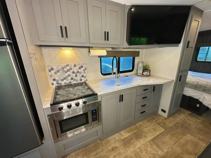 Modern RV rental kitchen with stove, microwave, sink, refrigerator, and TV. Ideal for comfortable on-the-go living.. Forest River Solera 2021