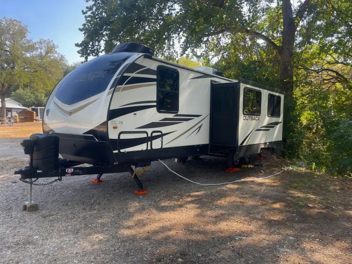Spacious Outback RV rental ready for your adventure. Parked on gravel, nestled among trees.. Keystone Outback 2022