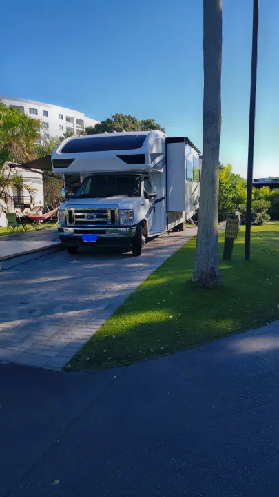 Relaxing RV rental setup at a sunny park: white motorhome on pavers, with an awning, hammock, and green grass.. Jayco Greyhawk 2023