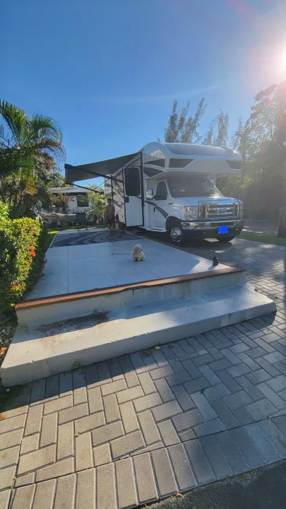 Bright RV rental campsite with extended awning, person, & a small dog on a sunny day.. Jayco Greyhawk 2023