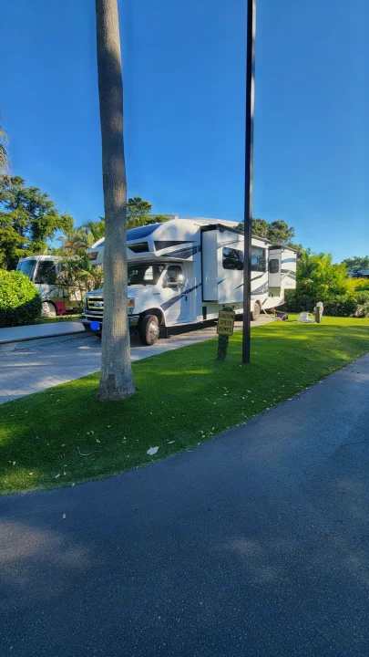 A spacious white rv rental motorhome is parked at a sunny resort site, with slide-outs extended, surrounded by green grass and trees.. Jayco Greyhawk 2023