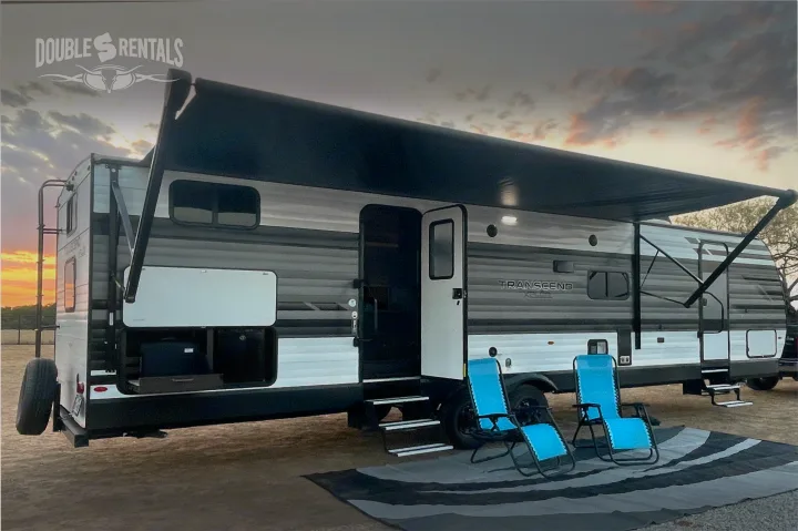 RV rental: A spacious gray and white travel trailer with an extended awning, two blue lounge chairs, and an outdoor mat at sunset.. Grand Design Transcend 2022