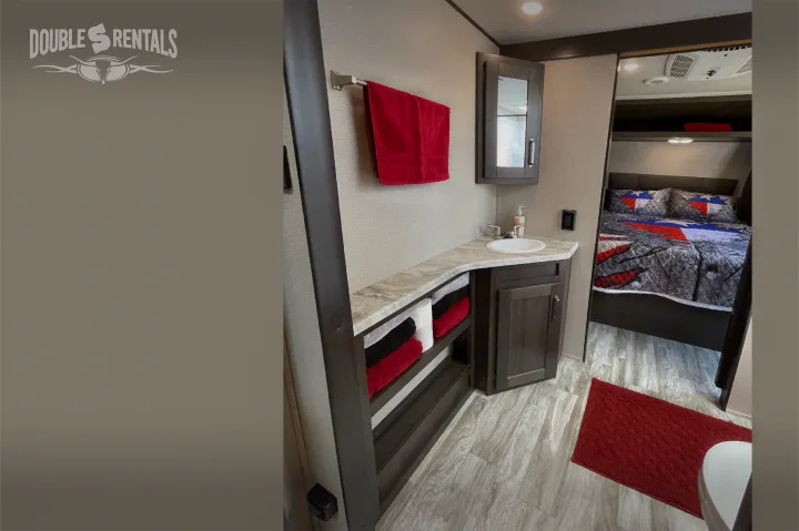Clean RV rental interior showing a well-appointed bathroom vanity with sink & towels, plus a comfortable bedroom beyond.. Grand Design Transcend 2022