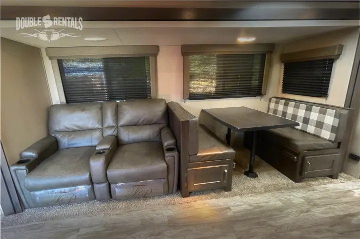 RV rental interior with a comfy recliner sofa and dining booth featuring a table and checkered backrest.. Grand Design Transcend 2022