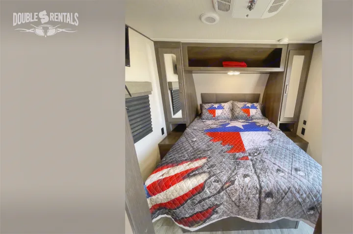 Cozy RV rental bedroom featuring a patriotic Texas flag and American flag quilt, with convenient overhead storage.. Grand Design Transcend 2022