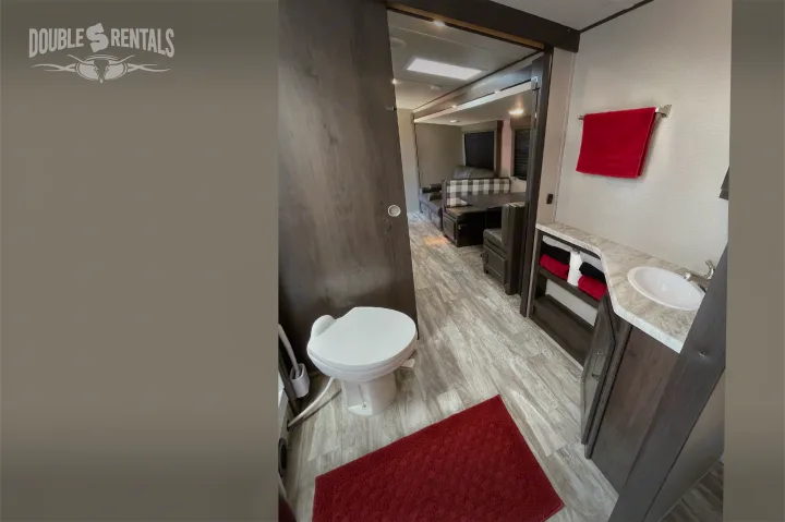 Discover this **RV rental** interior: a bright bathroom with toilet, sink, and a view into the inviting living area featuring a dinette and sofa.. Grand Design Transcend 2022