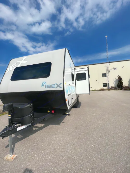 White Ibex travel trailer, great for an RV rental, parked on asphalt with its door open under a blue sky.. Forest River IBEXMBS 2023