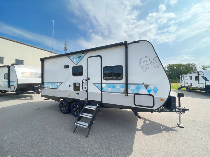 A modern white travel trailer with blue & grey geometric patterns, steps deployed, parked on asphalt. A perfect option for RV rental.. Forest River IBEXMBS 2023