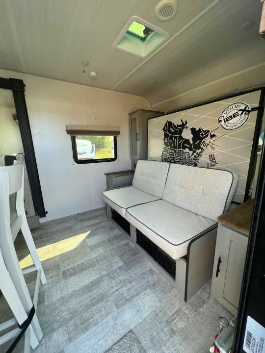 This RV rental features a cozy interior with a modern sofa, wood-look floor, and a Canada map mural.. Forest River IBEXMBS 2023