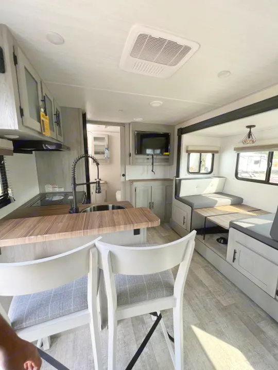 Spacious RV rental interior: modern kitchen counter with bar stools, dining booth, and TV area. Perfect for travel!. Forest River IBEXMBS 2023