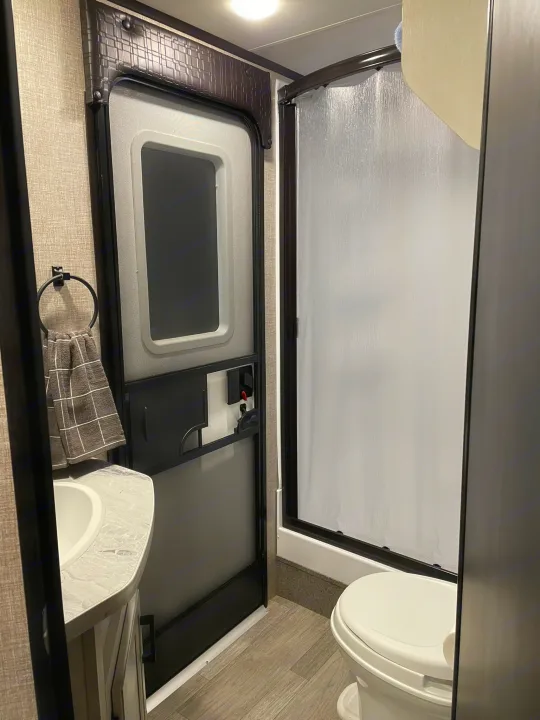 Compact RV rental bathroom with a sink, shower, and toilet, seen from the main living area, optimizing space.. Jayco Jay Feather 2022