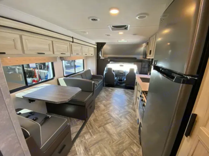 Bright, modern rv rental interior with a spacious dinette, full kitchen, and comfortable overhead bunk bed.. Forest River Sunseeker SLE 2023