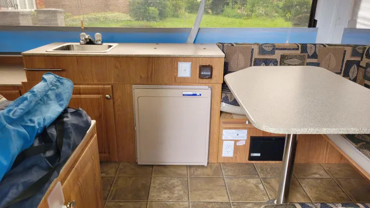 RV rental interior: A compact camper kitchen with a sink, small fridge, and dining area featuring patterned cushions.. Jayco 1207 2008