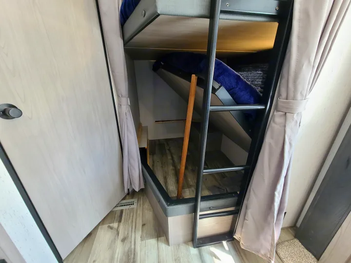 RV rental bunk beds: a ladder, privacy curtains, and cozy space with wood-look flooring.. Dutchmen Coleman 2022