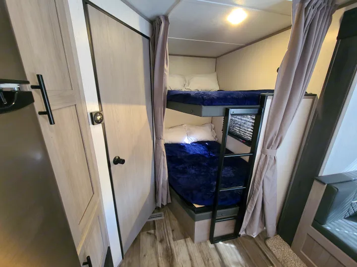 Cozy RV rental interior with bunk beds, dark blue bedding, a ladder, and privacy curtains for extra sleeping.. Dutchmen Coleman 2022