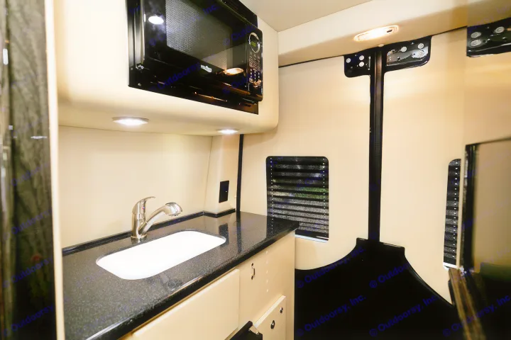 RV rental interior: Compact kitchen with sleek microwave, sink, and black countertop. Brightly lit for easy use.. Ultimate Toys Ultimate Coach 2024