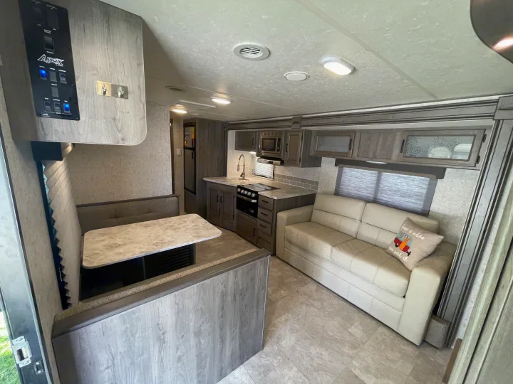 Spacious, modern RV rental interior with a living area, kitchen, and dining booth, perfect for comfortable travel.. Coachmen Apex 2019