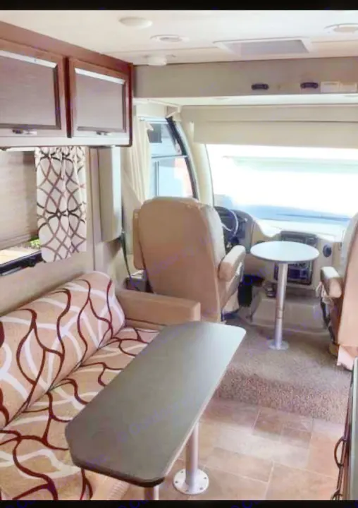 This RV rental interior features comfortable lounge seating, a dining table, and a functional driver's cockpit.. Thor Vegas 2016
