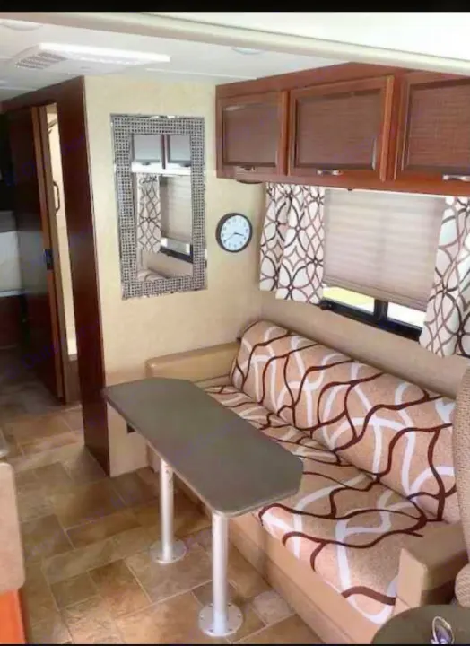 Inside this RV rental: a cozy living space with a patterned sofa, dinette table, cabinets, mirror, and tiled floor.. Thor Vegas 2016