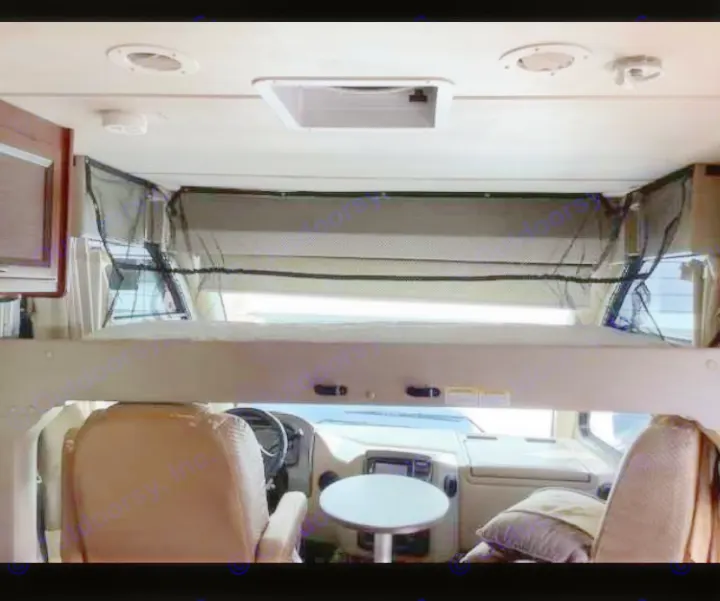 Inside an RV rental: an over-cab bunk bed with a mesh safety net, overlooking the driver's area and seating.. Thor Vegas 2016