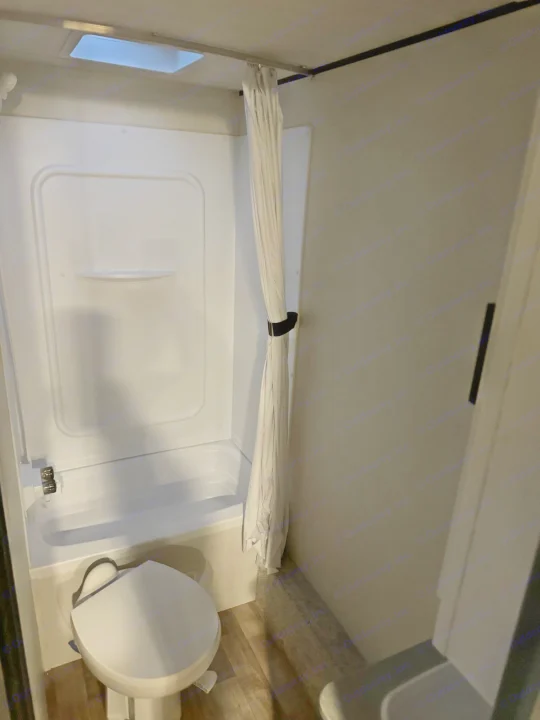 Inside an RV rental bathroom: features a compact shower/tub combo, toilet, and ceiling skylight for light.. keystone hideout 2022